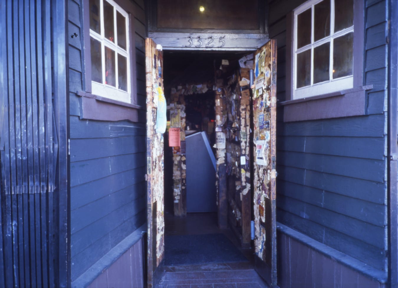 an open doorway into a music venue covered in stickers, flyers, and photos